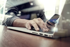 designer hand working and smart phone and laptop on wooden desk in office with london city background